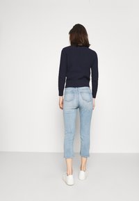 Suéter de punto azul marino con dobladillo acanalado, combinado con jeans cortos de color azul claro y zapatillas blancas; vista trasera que muestra texturas suaves y ajuste.