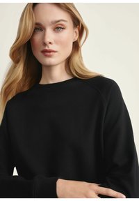 Czarna bluza z okrągłym dekoltem i rękawami raglanowymi. Miękka tekstura materiału, dopasowane mankiety i prosty design bez widocznych wzorów.