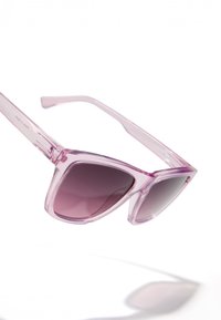 Rozā caurspīdīgi saulesbrilles ar ģeometrisku kaķa acu formu un gradientā pelēkiem stikliem. Rāmji ir gludi un spīdīgi, bez redzamas aparatūras.
