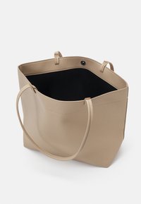 Sac cabas en cuir beige texturé avec doublure intérieure noire, deux fines bretelles et fermeture à bouton-pression sur fond blanc.