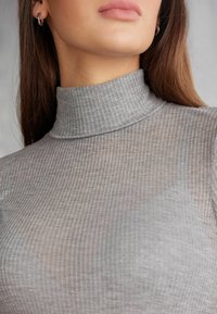 Šedý žebrovaný rolák s těsným střihem a texturovaným povrchem, který má vysoký límec a dlouhé rukávy.