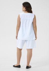 Top sans manches rayé bleu clair et blanc avec un dos froncé, associé à un short assorti, porté avec des chaussures plates noires.