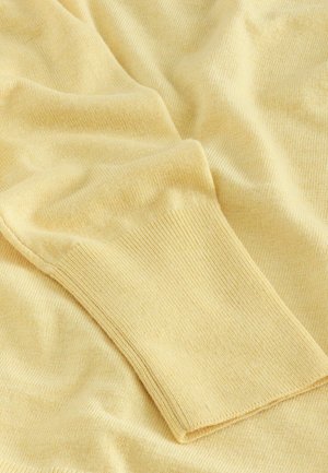 Light yellow knit fabric with a soft texture, featuring a ribbed cuff. Gentle folds and drapes are visible throughout the material.