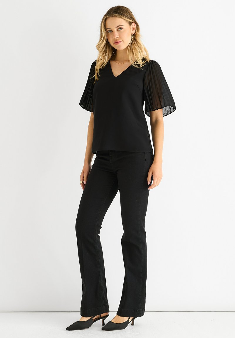 Black top with a V-neck and sheer pleated short sleeves, paired with matching black flared pants and pointed-toe black heels.