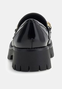 Czarne lakierowane buty ze skórzaną, zaokrągloną tylną częścią, grubą czarną podeszwą typu platforma oraz złotym ozdobnym elementem na pasku. Podeszwa teksturowana dla lepszej przyczepności.