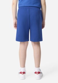 Sinised puuvillased lühikesed püksid elastse vöökohaga ja taskutega, kantud valgete tossudega, millel on punased detailid, ning valgete sokkidega.