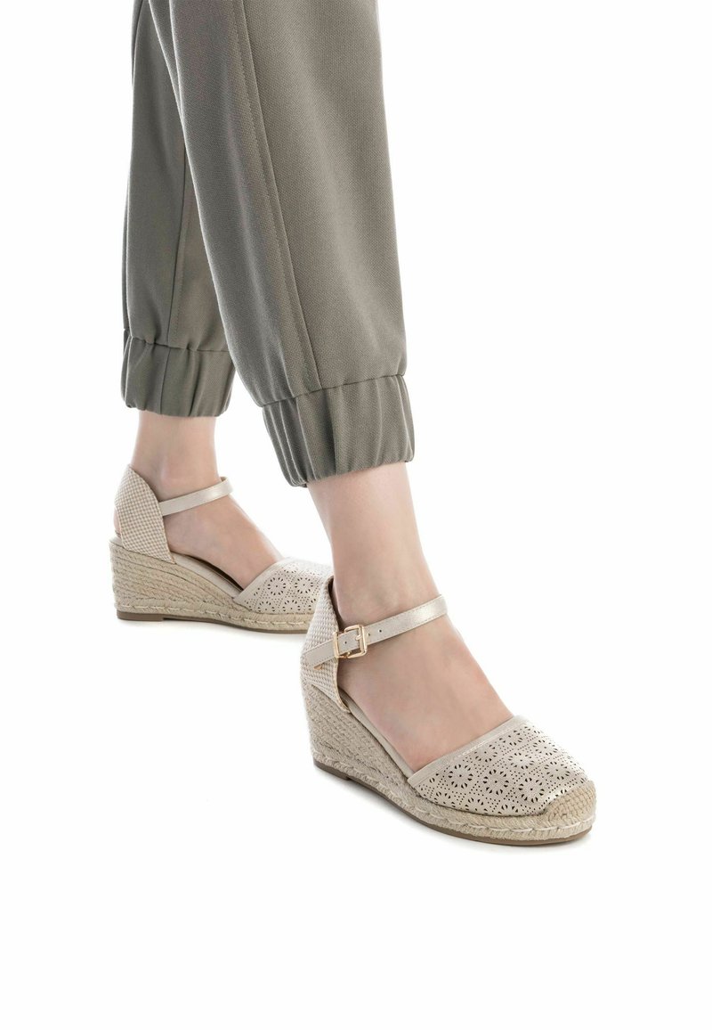 Sandalias de cuña beige con un diseño superior perforado. Cuentan con una correa en el tobillo y detalles de yute trenzado en el tacón de cuña. Elegantes y ligeras.