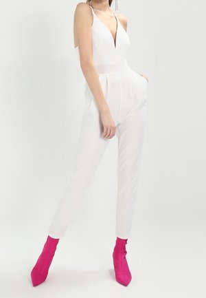 Hvid jumpsuit med dyb udskæring, tætsiddende overdel og affasede ben. Sammen med klare pink stiletto ankelsko. Glat tekstur.