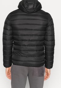 Svart vadderad jacka med huva, med ett quiltat mönster och horisontella linjer. Materialet ser blankt och slätt ut; minimal detaljering.