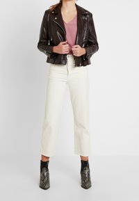 Ruskea nahkainen moottoripyörätakki, vaaleanpunainen paita, kermaisen väriset leveälahkeiset housut ja mustat saappaat, joissa on käärmeennahkakuosi ja korkeat korot.