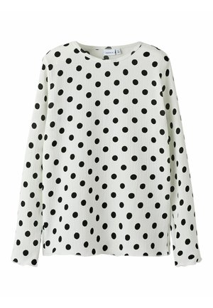 Chemise à manches longues blanche avec des pois noirs. Col rond, tissu texturé et fentes sur les côtés pour plus de liberté de mouvement.