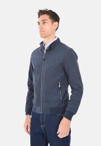 Giacca bomber blu navy in tessuto testurizzato, con colletto alto, due tasche frontali con zip e polsini in maglia alle aperture delle maniche.