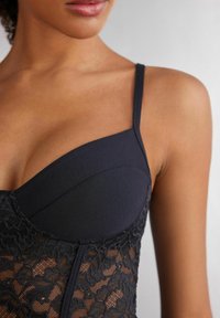 Svart spetsbodysuit med texturerad spets på den nedre delen, slät tyg på den övre delen och tunna justerbara band.