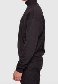 Sudadera negra con cuello alto, que presenta mangas largas y un corte relajado. Fabricada con material suave, con puños y dobladillo de canalé.