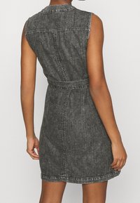 Sleeveless black denim dress with a fitted waist, belt detail, and stitching accents. Back view shows a straight cut and textured finish.
