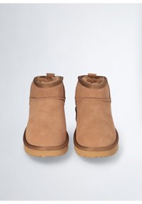 Stivali ankle in suede color tan con una morbida fodera in pelliccia, punta rotonda e suola in gomma. Presentano un tacco basso e accenti di cucitura a contrasto.