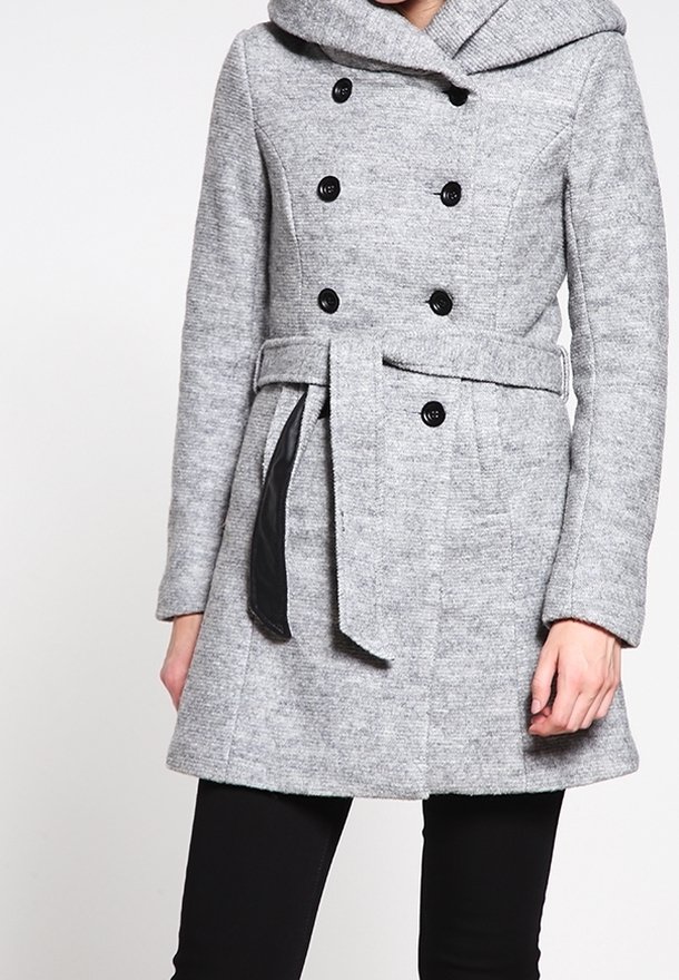 Grå dubbelknäppt ullkappa med svarta knappar, bälte vid midjan och huva, bärs med svarta byxor.