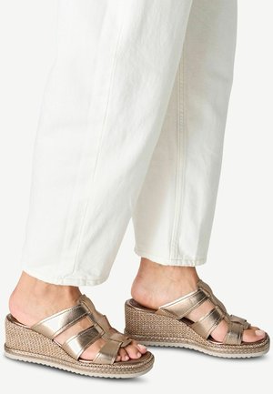 Metallische bronzen platform sandalen met een geweven jute zool, brede overlappende banden, open neus en een rugloze ontwerp, gecombineerd met witte broek.