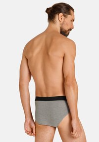 Slip in cotone grigio da uomo con una vita elasticizzata nera, caratterizzati da un design aderente e una texture liscia, visti da un'angolazione posteriore.