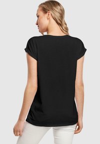 Schwarzes T-Shirt mit kurzen Ärmeln und umgeschlagenen Ärmeln, aus leichtem Stoff, lässiger Schnitt und glatter Textur, getragen mit weißen Hosen.