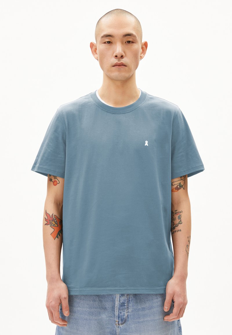 Lichtblauw katoenen t-shirt met ronde halslijn, korte mouwen en klein wit logo op de borst. Draagt bij een denim korte broek.