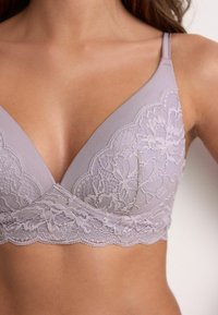 Sutien lavandă cu dantelă aplicată cu modele florale, cupe triunghiulare, bretele reglabile și margini festonate. Textură moale, design fără cusături.