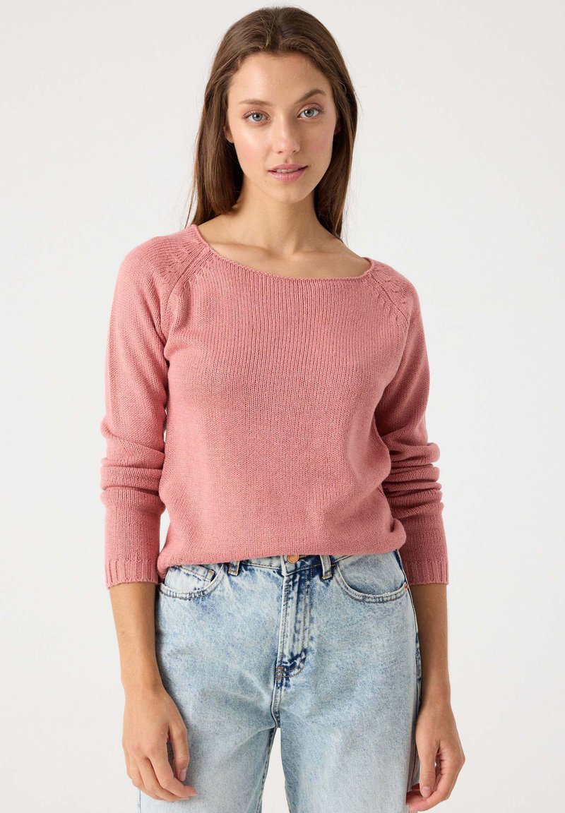 Suéter de punto rosa con escote cuadrado y puños acanalados, combinado con jeans de tiro alto en azul claro. Textura suave y corte relajado.