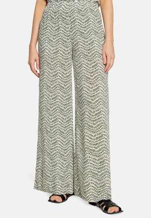 Person wearing wide-leg, high-waisted pants with a black and white wavy dotted pattern and black sandals, cropped from chest down.