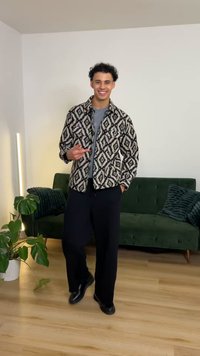 Fekete-fehér mintás dzseki gyémántmotívumokkal, szürke ing fölött viselve, laza fekete nadrággal párosítva. Zöld kanapé a háttérben.