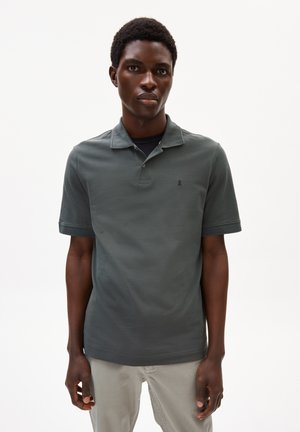 Polo shirt gris foncé à manches courtes avec un col, présentant un logo brodé discret sur la poitrine et un tissu texturé. Design sobre.