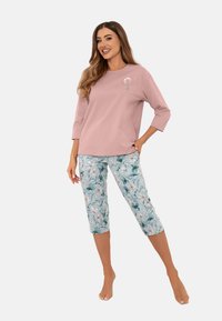 Jasnoróżowa bluzka z długim rękawem z kwiatowym haftem; połączona z krótkimi spodniami w kwiatowy wzór w odcieniach niebieskiego i zielonego.