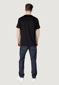 Zwart katoenen T-shirt met een ronde hals, gecombineerd met donkerblauwe spijkerbroek en witte sneakers. Eenvoudig ontwerp, zonder opvallende patronen of accenten.