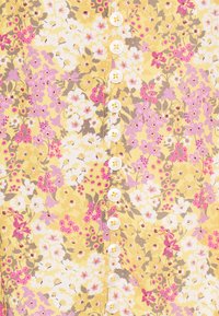 Tessuto floreale giallo con fiori rosa e bianchi, accentuato da una fila di sei bottoni bianchi al centro. Texture liscia.