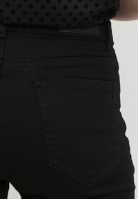 Fekete farmernadrág, testhez simuló fazonnal, egyetlen hátsó zsebbel, finom textúrával, és prominent hardware vagy díszítés nélkül.