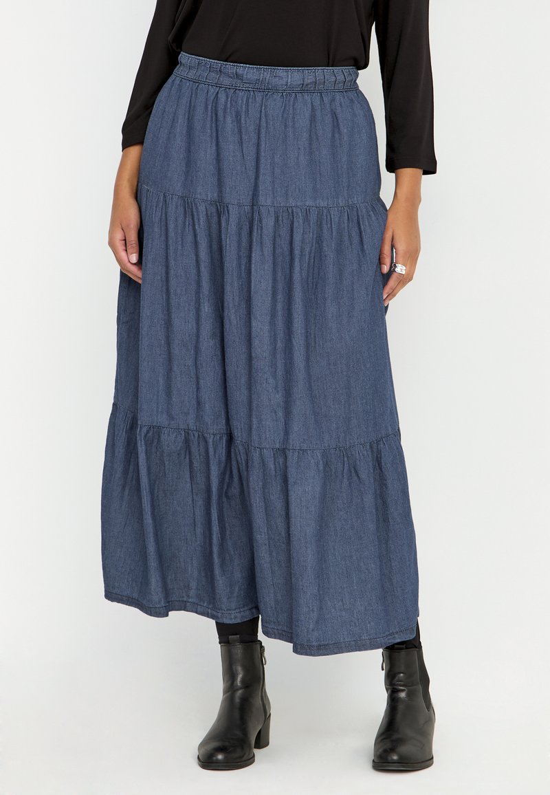 Denim maxikjol med tre lager volanger, elastisk midja och en djupblå färg; tillsammans med svarta ankelboots.