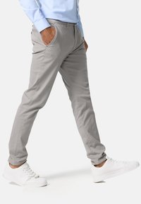 Pantalon slim gris clair en mélange de coton. Doté de poches latérales, de jambes légèrement fuselées, et porté avec des chaussures blanches à lacets.