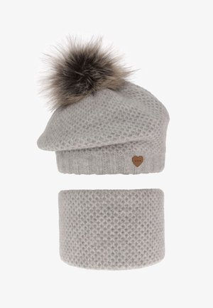 Gebreide grijze muts met een pluizige pompon en een klein hartje als accent. Gecombineerd met een bijpassende, gestructureerde grijze nekwarmer.