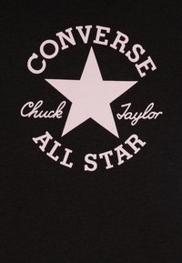 Juodas marškinėliai su baltu žvaigždės logotipu, viršuje yra užrašas "Converse", o apačioje - "Chuck Taylor All Star" boldiniu, apvaliu šriftu. Minkšta medžiagos tekstūra.