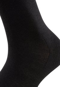 Krupni plan crne pamučne čarape do gležnja koja prikazuje teksturu i oblik na bijeloj pozadini.