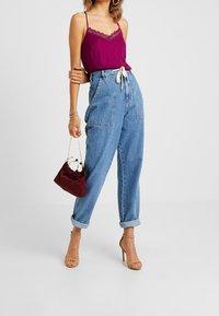 Camisola magenta con bordi in pizzo, pantaloni in denim blu chiaro a vita alta con risvolti e una borsa in tessuto borgogna con tracolla a catena.