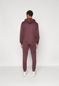 Moletom marrom e calças de jogger feitas de tecido macio, com capuz, punhos canelados e um corte slim. Usado com ténis brancos.