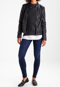 Mustat keinonahkainen takki, jossa on vetoketju, ribattu pinta; yhdistetty tummiin farkkuihin ja kerrokselliseen harmaaseen neuleeseen, jossa on valkoinen helma. Mustat loaferit.