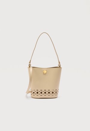 Geantă tip sac din piele bej, cu o curea lungă, închizătoare aurie și model decorativ tăiat de-a lungul marginii inferioare, prezentată pe un fundal alb.