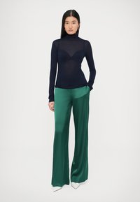 Marinblå polo med figurnära design, kombinerad med gröna satintyg vida byxor och vita spetsiga klackskor.