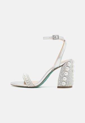 Zilveren sandaal met open teen, versierd met een parel op het bandje en een gebeeldhouwde blokhak met grote parels en een getextureerd oppervlak.