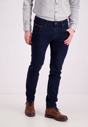 Vaqueros de mezclilla azul oscuro con un ajuste slim, cintura de altura media y costuras en contraste. Llevados con botas de cuero marrón.