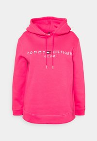 Różowa bluza z kapturem wykonana z bawełny, z naszywką z napisem "TOMMY HILFIGER" i "EST. 1985" wyszywanymi z przodu. Posiada kaptur z regulowanym sznurkiem.