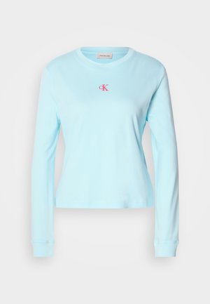 Lichtblauwe langemouwen shirt van zachte stof, met een ronde halslijn en een klein roze geborduurd logo op de borst.