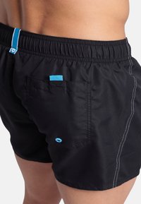Černé plavky s elastickým pasem, modrými akcenty, zadní kapsou a kontrastním bílým švem podél švů.