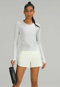 Haut de sport à manches longues gris clair en tissu texturé, complété par un short jaune néon et une bouteille d'eau noire avec un logo blanc.